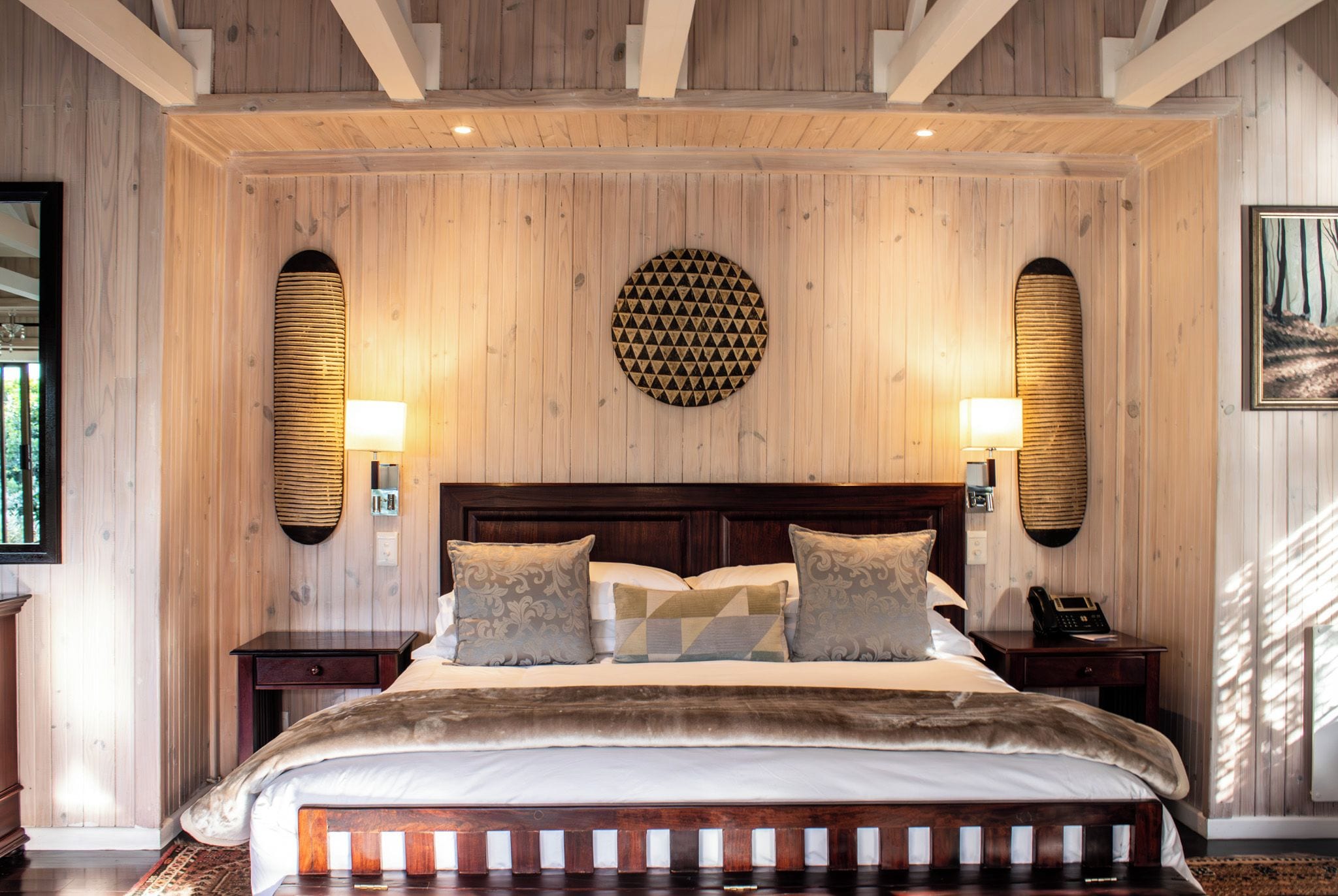 A bedroom with a large bed, wooden headboard, two bedside tables, and wall-mounted lamps.