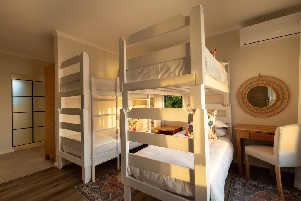 A room with bunk beds, a desk, a chair, a mirror, and a view of greenery outside.