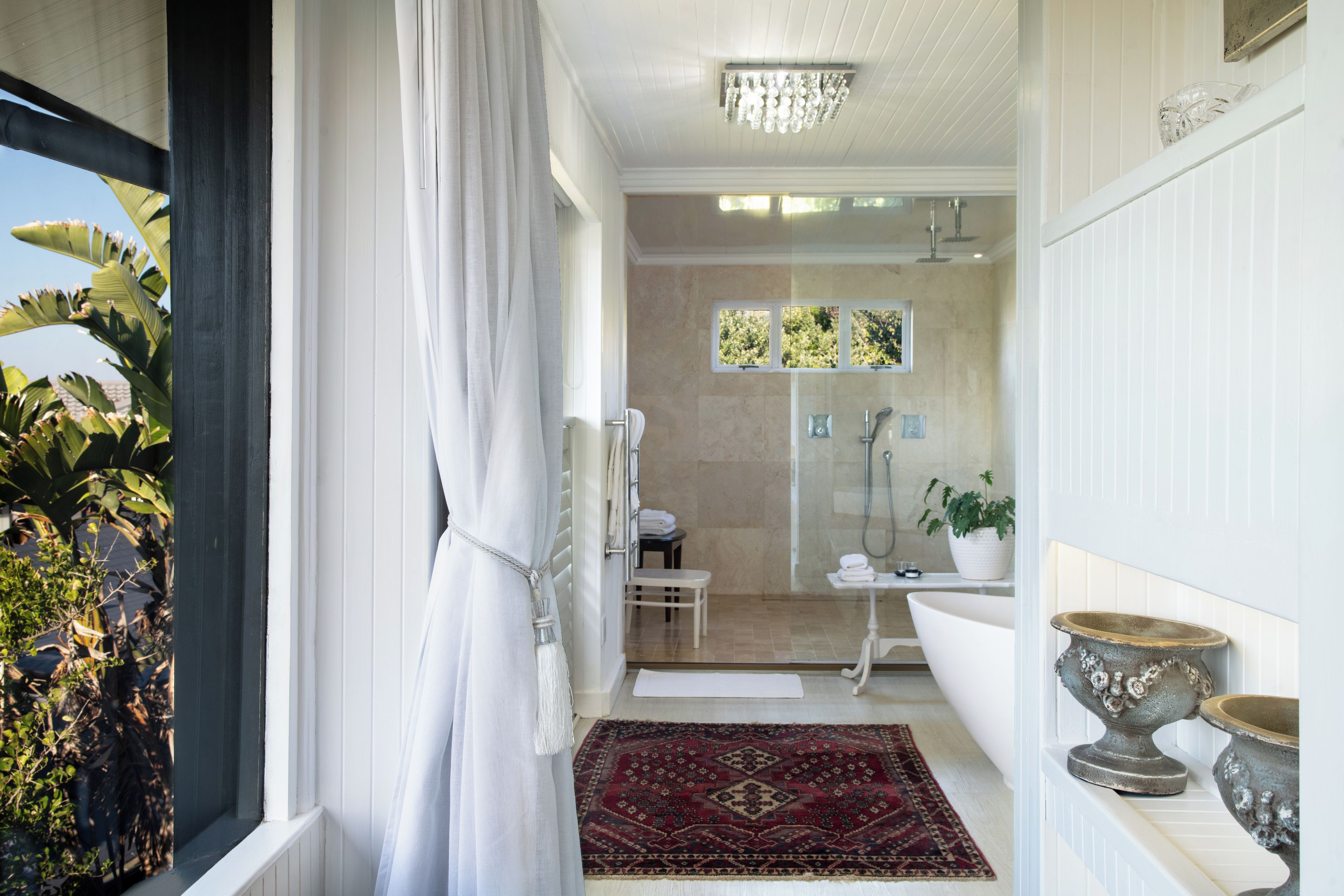 A bathroom with a shower, a sink, and a toilet. There is a window with a view of trees and a potted plant.