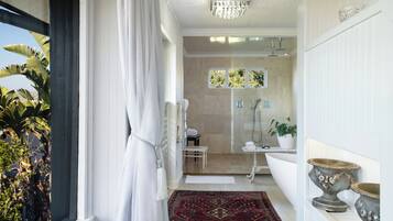 A bathroom with a shower, a sink, and a toilet. There is a window with a view of trees and a potted plant.