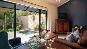 Una sala de estar moderna con un amplio ventanal corredizo que da a una zona de piscina, un mueble de madera, un televisor y una zona de estar acogedora con un sofá y sillones.