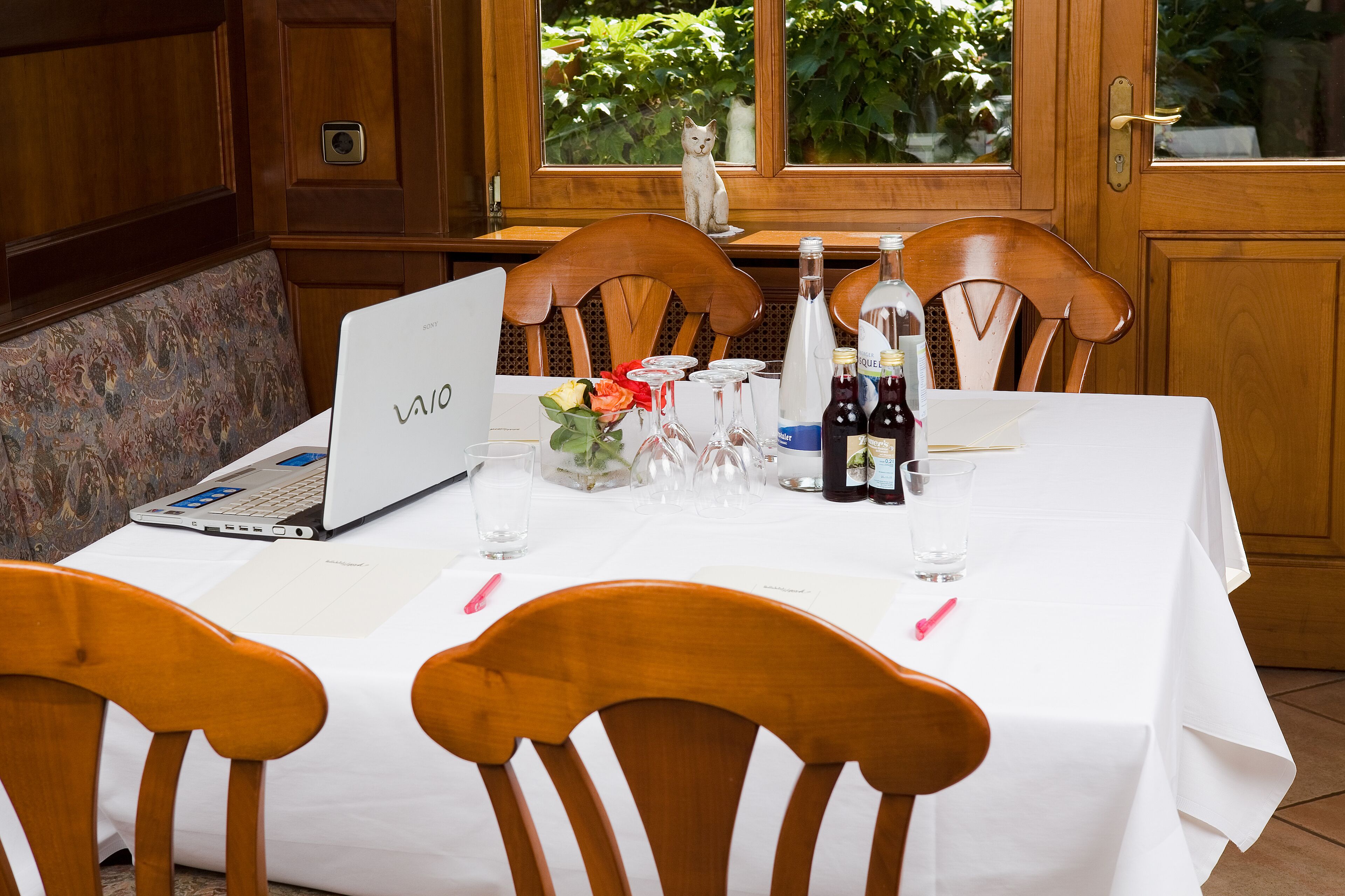 A dining table set with a laptop, wine bottles, glasses, and a vase with flowers.