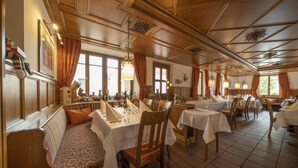 Un restaurante con paneles de madera, manteles blancos y un banco con cojines estampados.