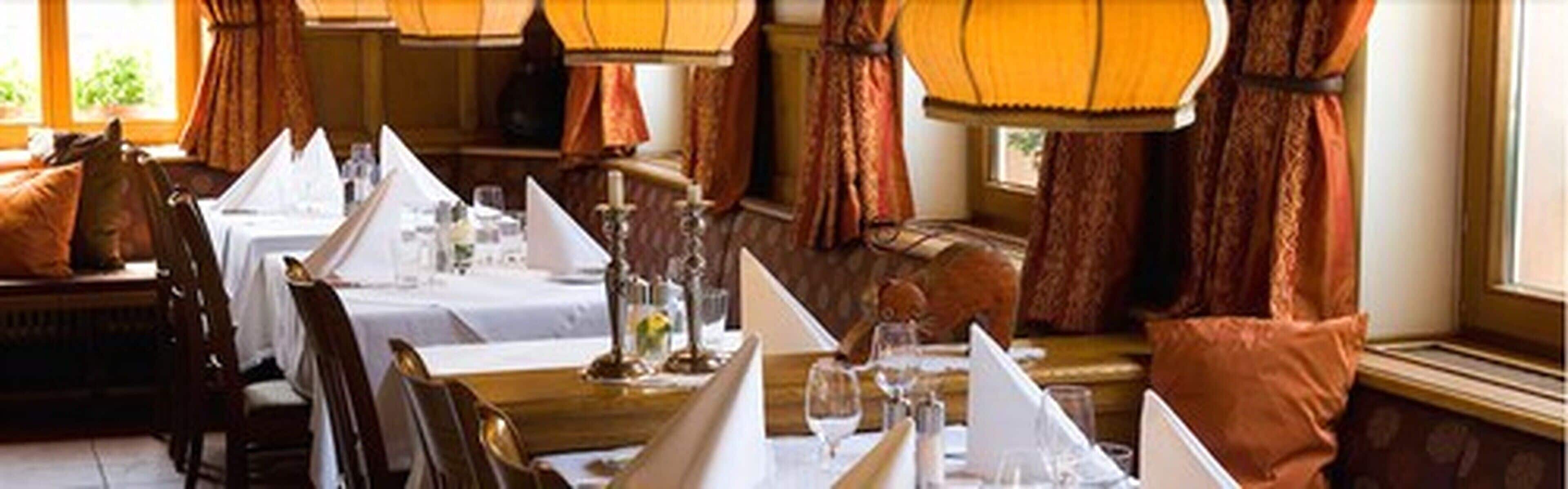 A restaurant with tables set for dining, featuring a classic interior design with curtains and warm lighting.