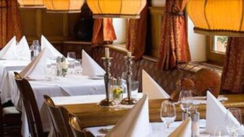 A restaurant with tables set for dining, featuring a classic interior design with curtains and warm lighting.