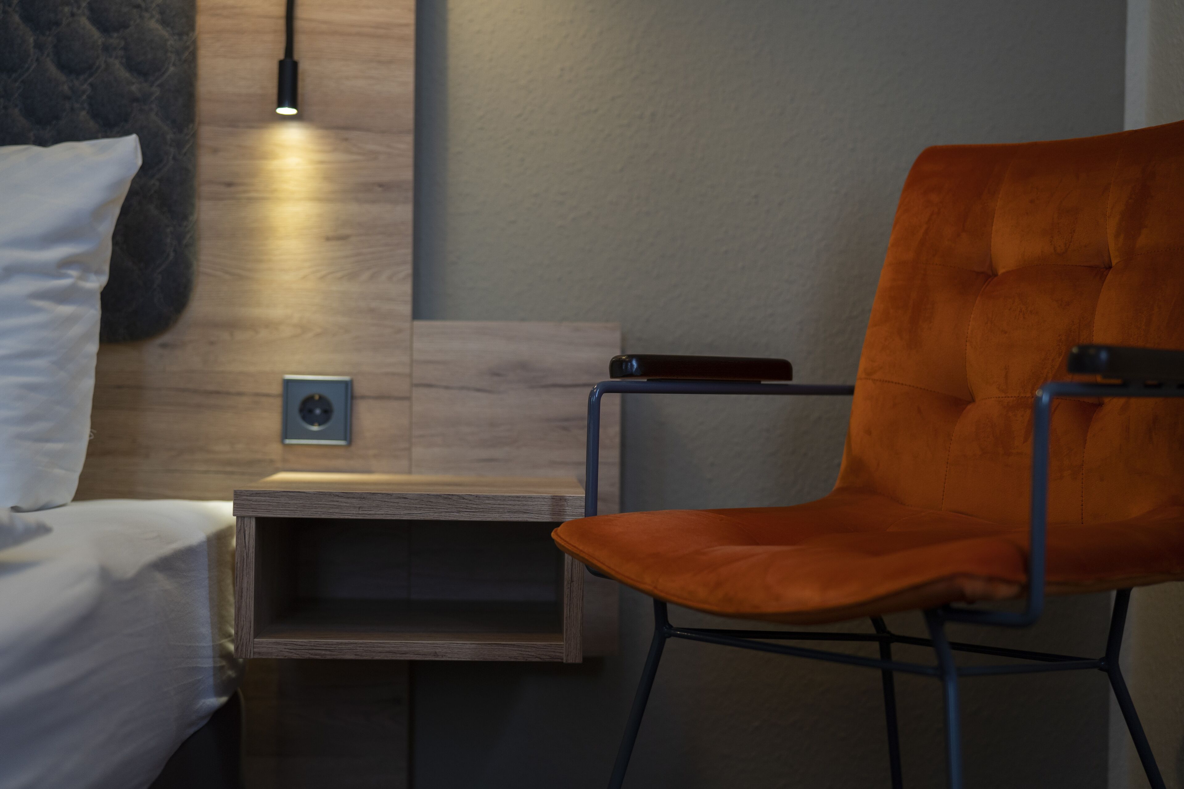 Une chambre moderne avec un lit, une table de chevet en bois, une petite table et une chaise orange.