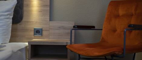Une chambre moderne avec un lit, une table de chevet en bois, une petite table et une chaise orange.