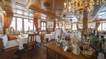 Un restaurante con mobiliario de madera, una zona de bar con diferentes botellas y un candelabro.
