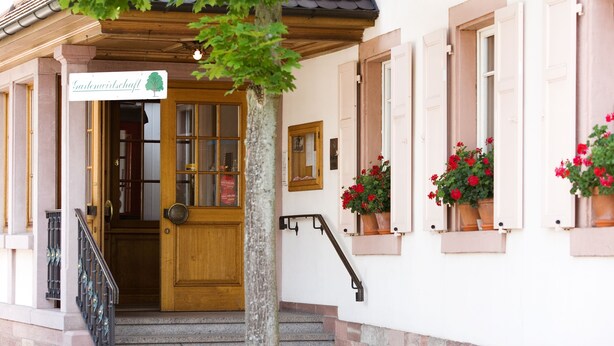 La entrada de un edificio con puerta de madera, una escalera y macetas en las ventanas.