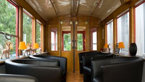 Interior de un vagón de tren con paneles de madera, asientos de cuero negro y ventanas con marcos rojos.