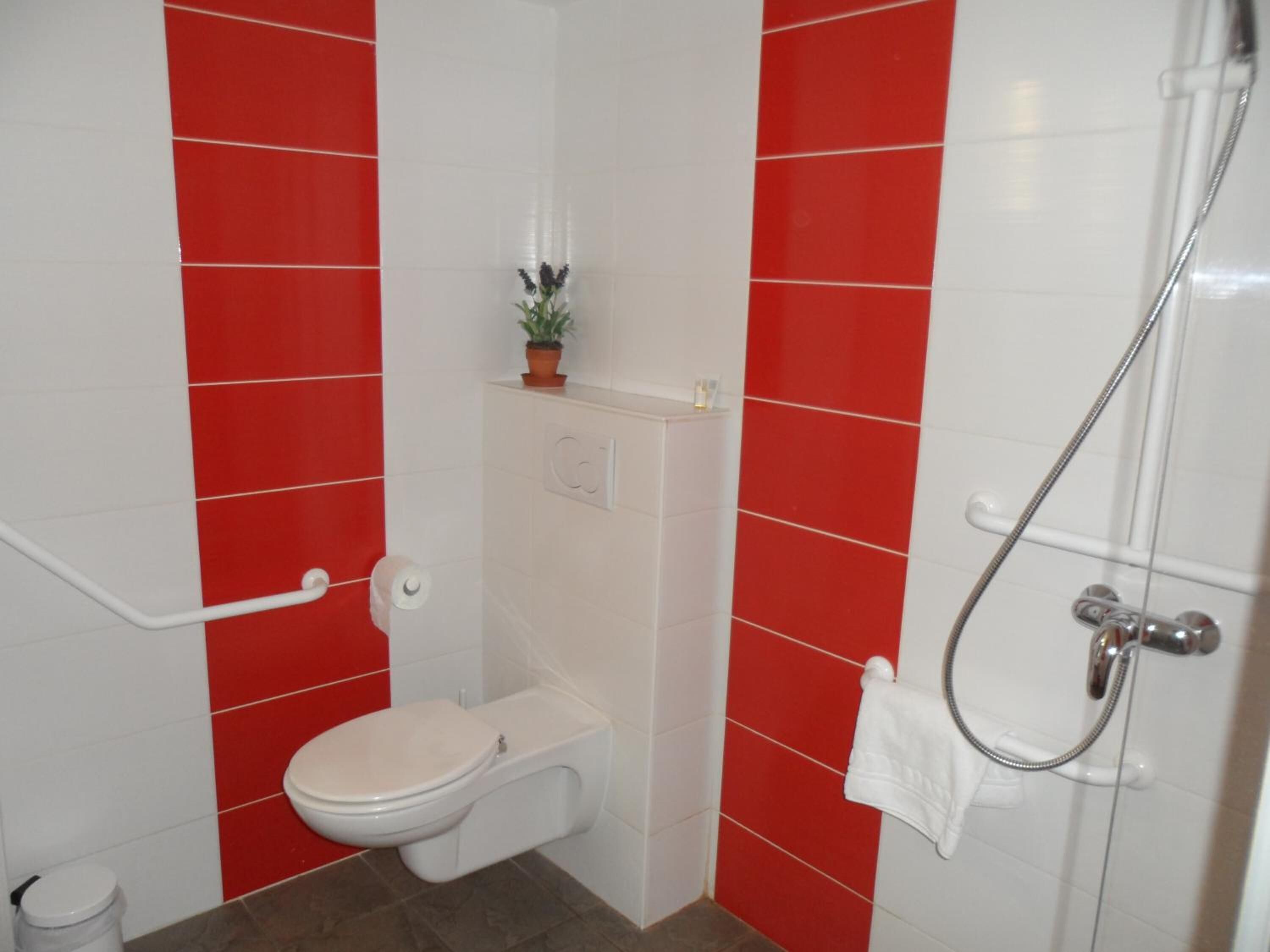 Um banheiro pequeno com vaso sanitário, chuveiro e parede revestida com azulejos vermelhos e brancos.