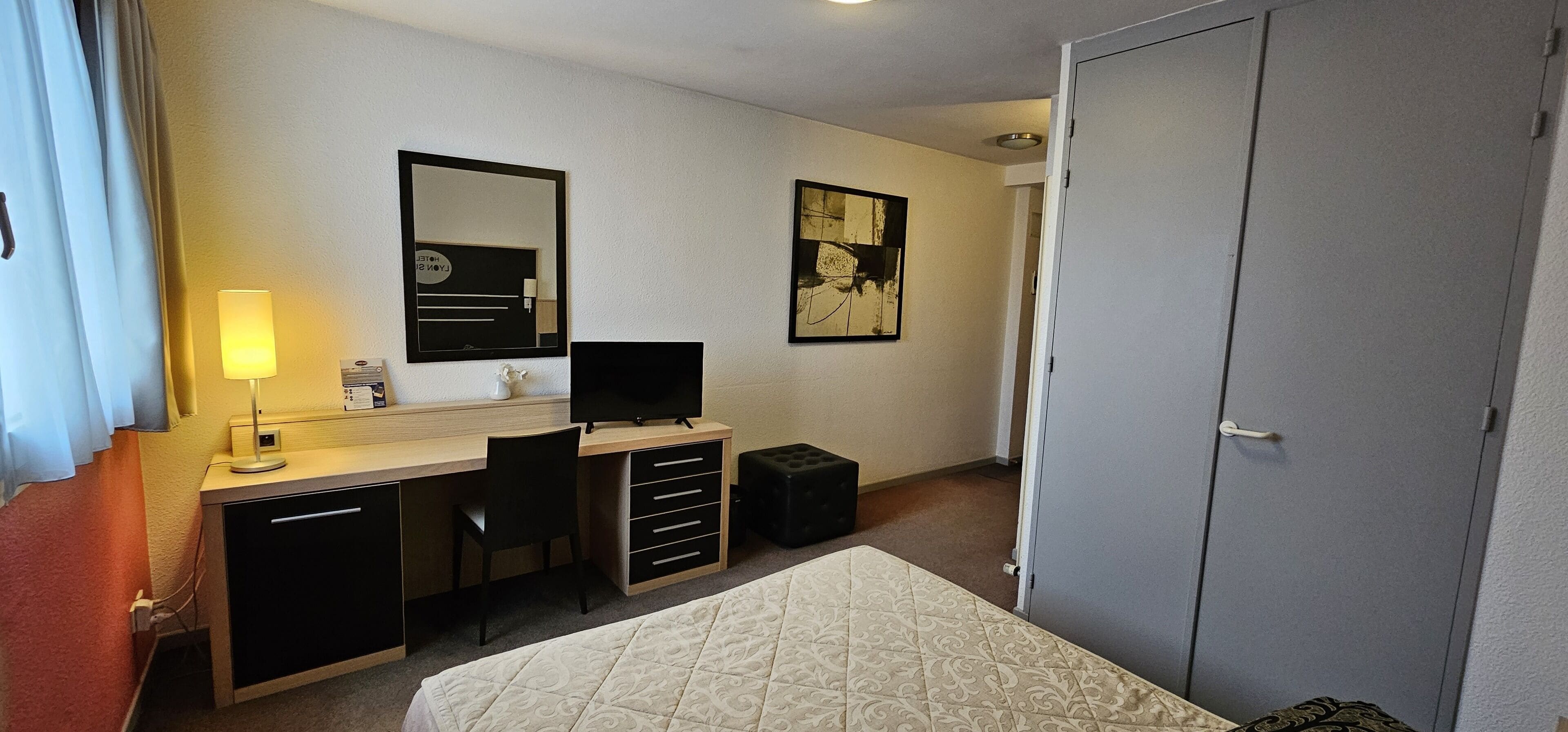 Une chambre d’hôtel équipée d’un lit, d’un bureau, d’une chaise, d’un ordinateur, d’une lampe et d’une armoire.