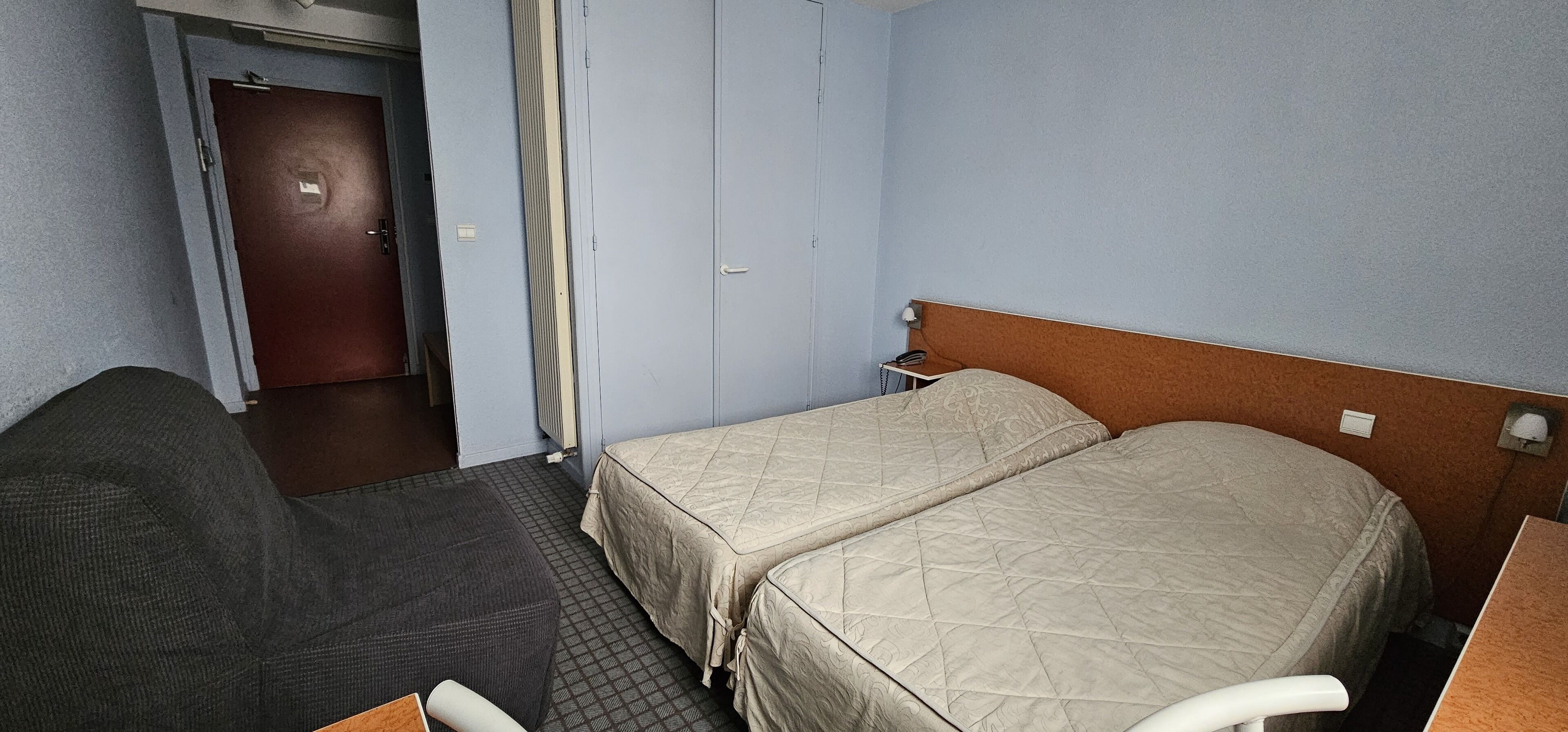 A hotel room with two beds, a desk, a chair, and a door.