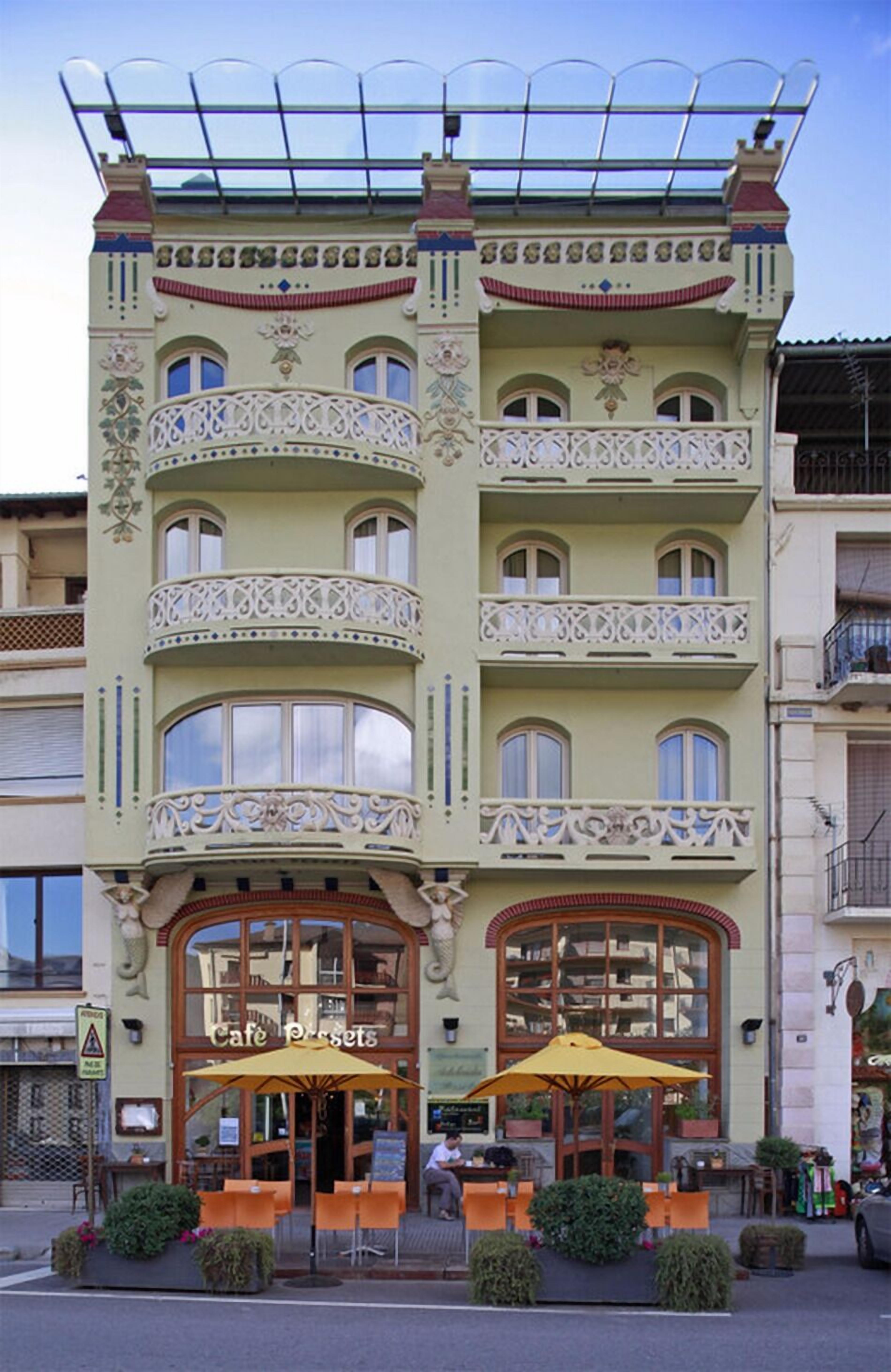 Un immeuble à plusieurs étages, doté de balcons décorés, de grandes fenêtres et d’un café situé au rez-de-chaussée.