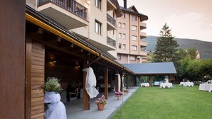 A hotel with a covered outdoor area, a grassy lawn, and tables set up for dining. - Hotel Pessets & Spa (Sort)