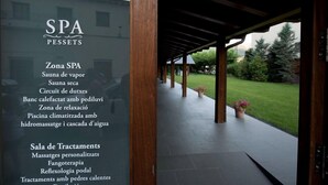 A spa area with a covered walkway, wooden pillars, and a view of a green lawn and trees. - Hotel Pessets & Spa (Sort)