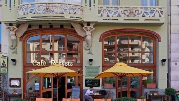 A cafe with outdoor seating and ornate architectural details. - Hotel Pessets & Spa (Sort)