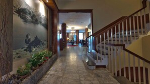 A hallway with a stone floor, a mural of a mountainous landscape, and a staircase with wooden railings. - Hotel Pessets & Spa (Sort)