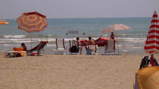Una playa con varias tumbonas y sombrillas, una torre de socorristas y el océano al fondo.