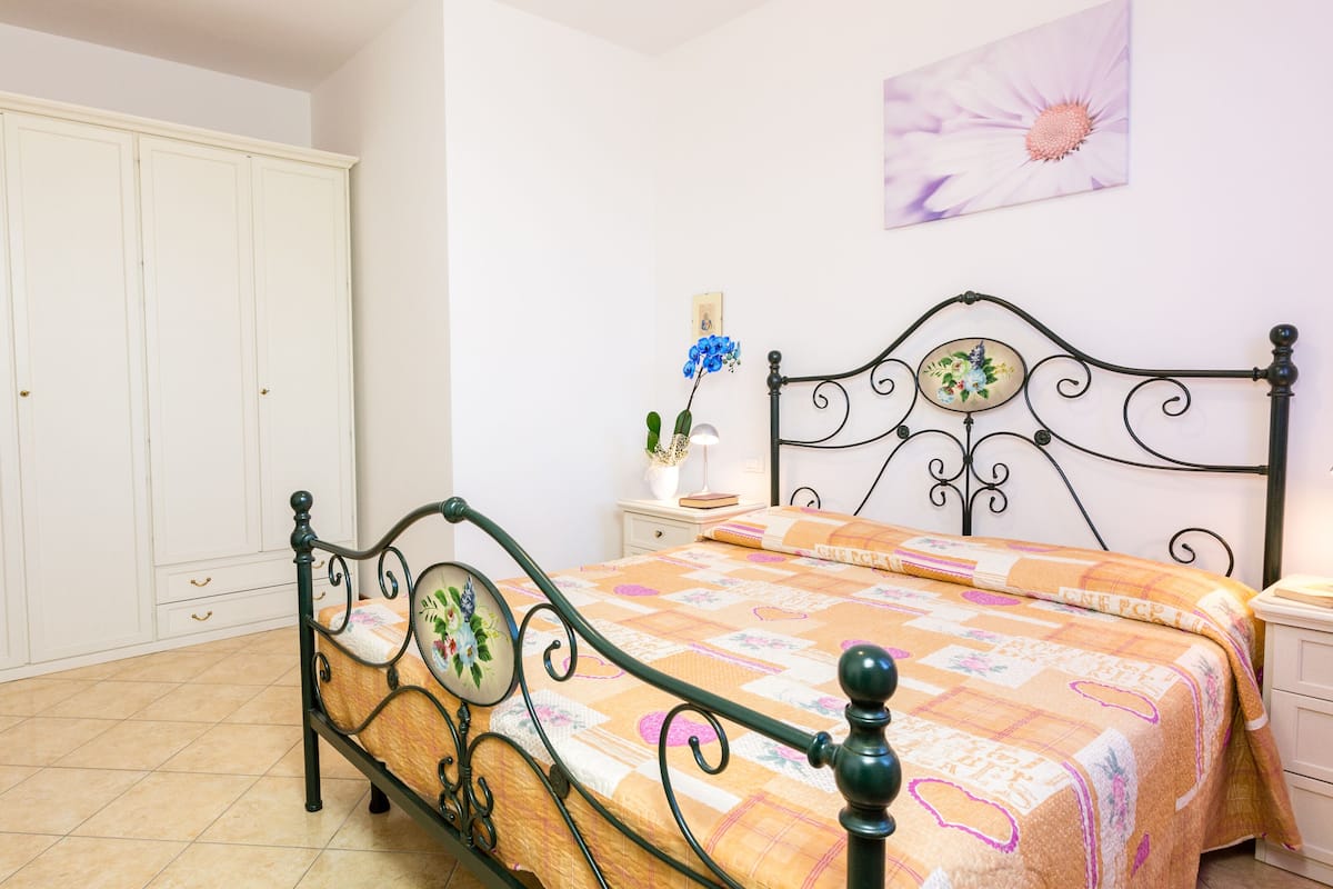 A bedroom with a bed, a wardrobe, a nightstand, and a wall-mounted lamp.