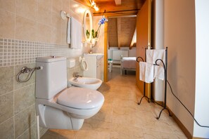 A modern bathroom with a toilet, bidet, and sink. There is a towel rack with towels and a small potted plant.