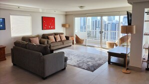A modern living room with a grey sofa, a red abstract painting, and a view of a cityscape through large sliding doors. - Marriner Views (Surfers Paradise)