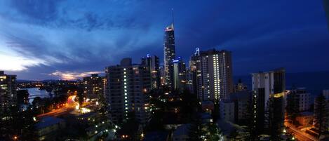 A cityscape at dusk with illuminated buildings and a river in the foreground.
