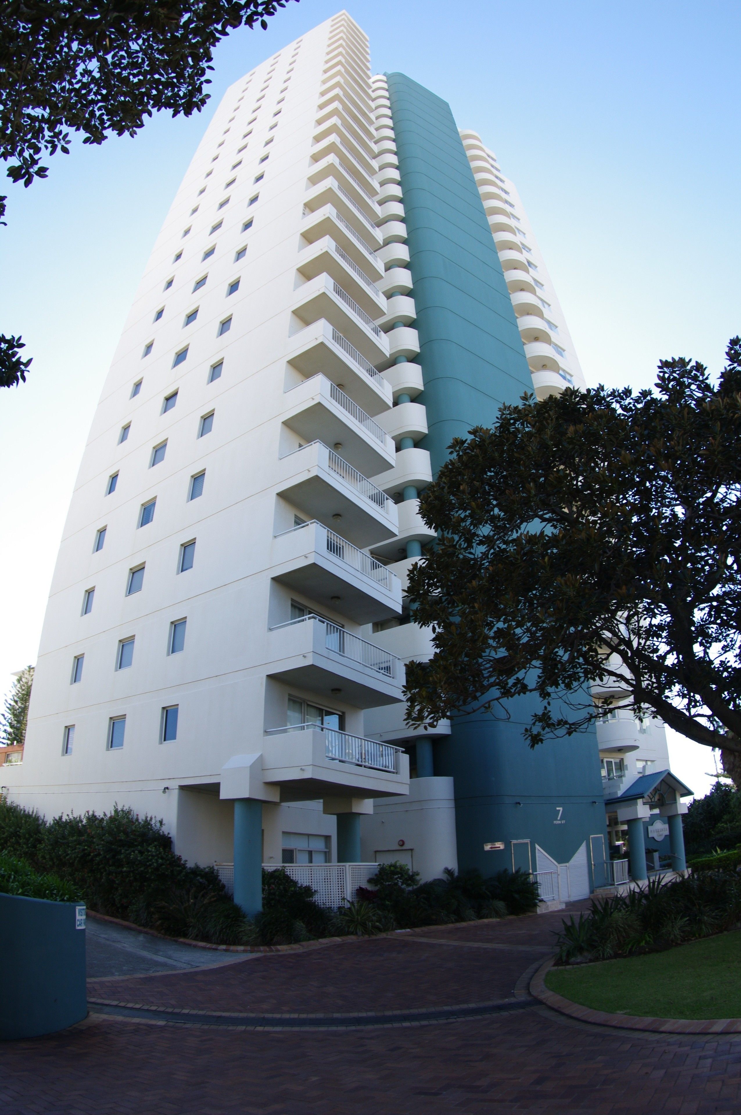 Ein hohes, mehrstöckiges Hotel mit einem markanten blau-weißen Farbdesign, das Balkone auf jeder Etage und eine gepflegte umliegende Landschaft aufweist.