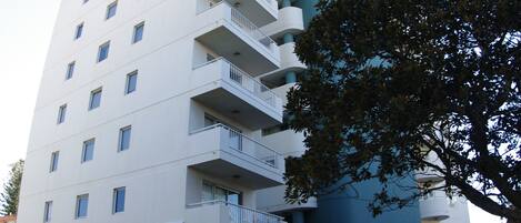 Ein hohes, mehrstöckiges Hotel mit einem markanten blau-weißen Farbdesign, das Balkone auf jeder Etage und eine gepflegte umliegende Landschaft aufweist.