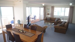 A spacious living area with a wooden dining table, brown sofas, and a glass coffee table. - Marriner Views (Surfers Paradise)