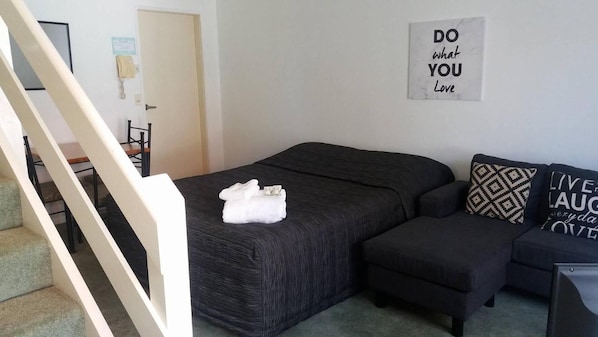 A bedroom with a bed, a small sofa, a staircase, and a motivational quote on the wall. - Baden Lodge Motel (Rotorua)