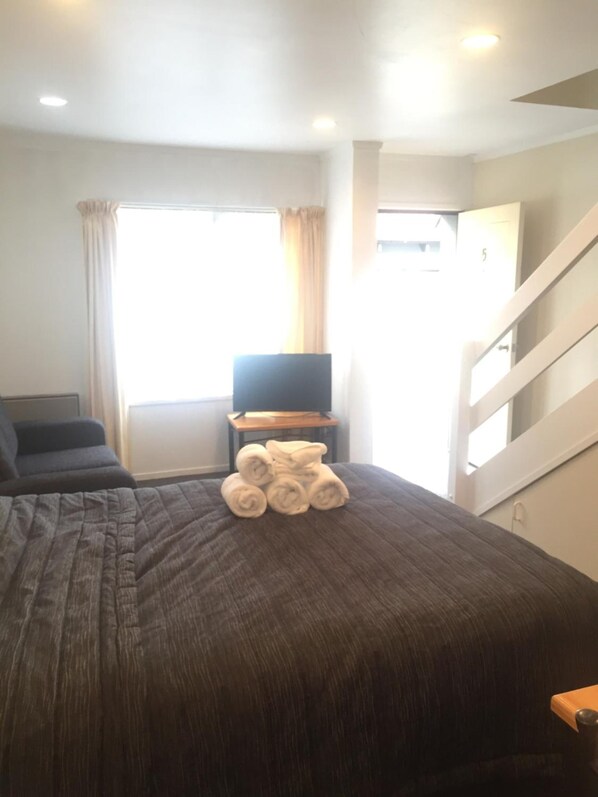 A hotel room with a large bed, a TV on a small table, and a staircase leading to another room. - Baden Lodge Motel (Rotorua)