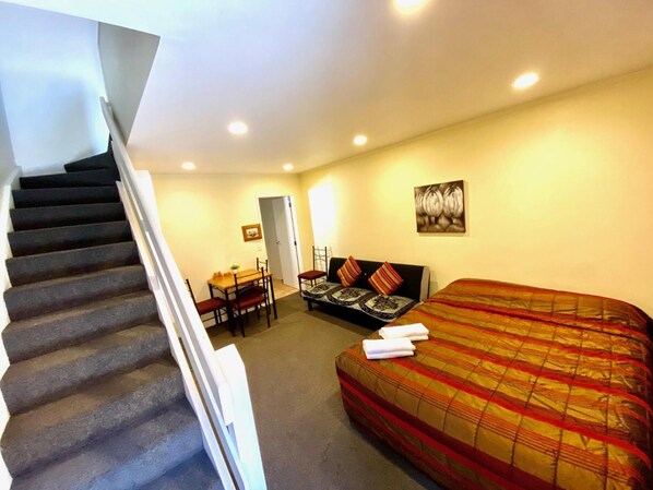 A bedroom with a bed, a sofa, a dining table, and a staircase. - Baden Lodge Motel (Rotorua)