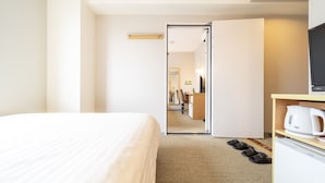 A hotel room with a bed, a desk with a computer, a coffee maker, and slippers on the floor.