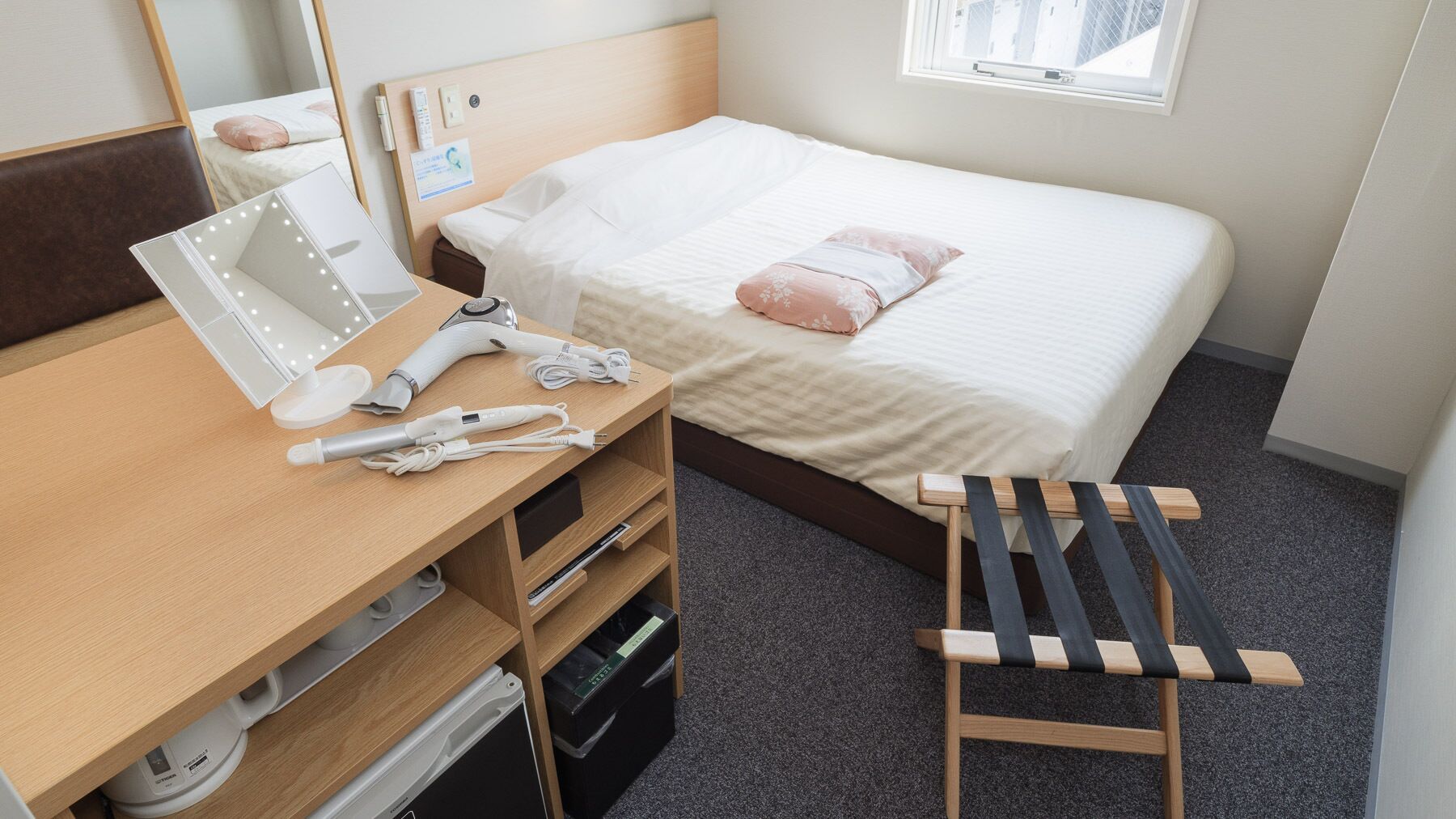 Habitación de hotel con una cama, un escritorio con espejo, un secador de pelo y un taburete pequeño.