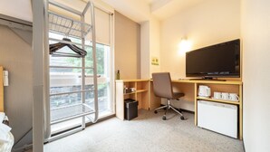 A hotel room with a desk, chair, TV, and a small kitchenette.