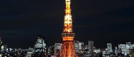 Vista noturna de uma paisagem urbana com uma torre iluminada em destaque.
