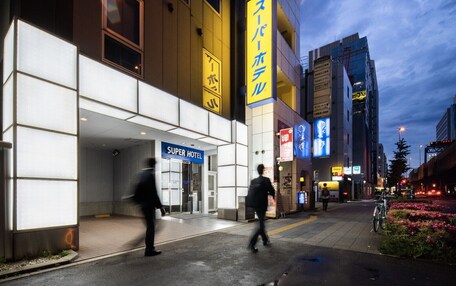 A hotel with a modern facade, a prominent 'Super Hotel' sign, and a pedestrian walkway with flowers.