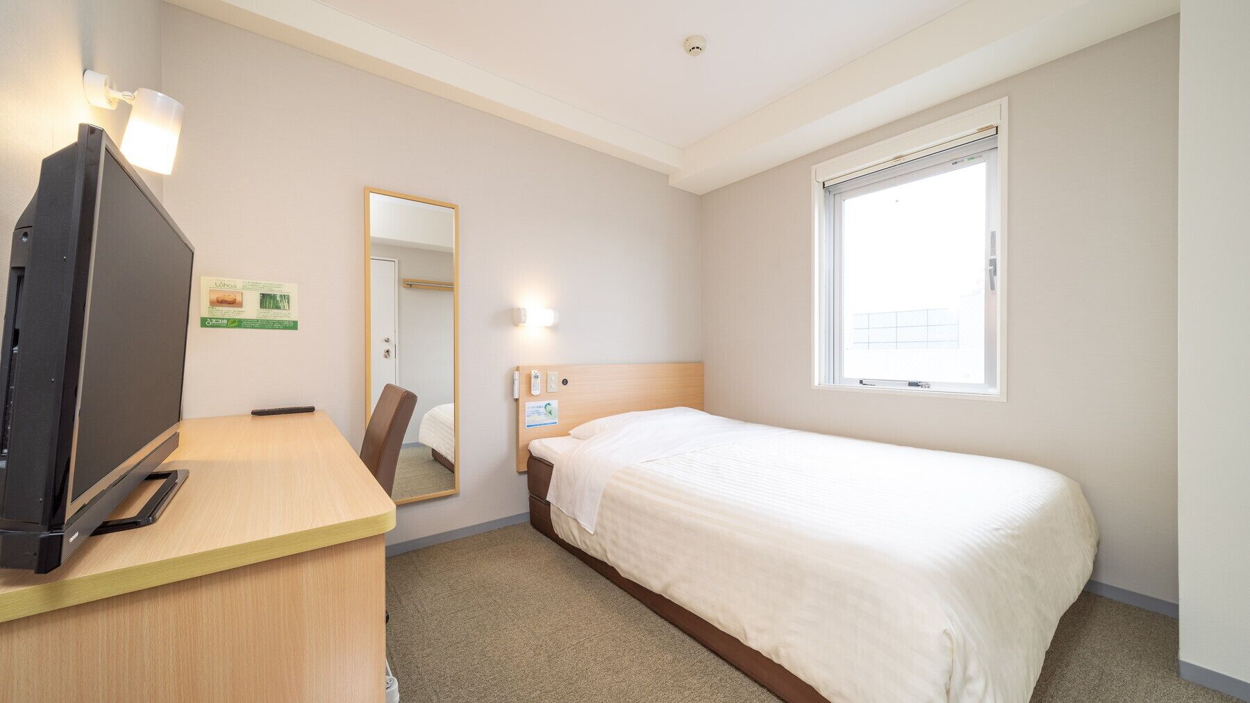 A hotel room with a bed, a desk with a television, a mirror, and a window.