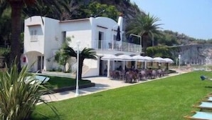 A white building with a balcony, surrounded by a well-maintained lawn and palm trees. - Villa Angelina (Massa Lubrense)