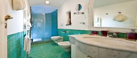 A bathroom with a large mirror, two toilets, a shower, and a sink with a marble countertop.