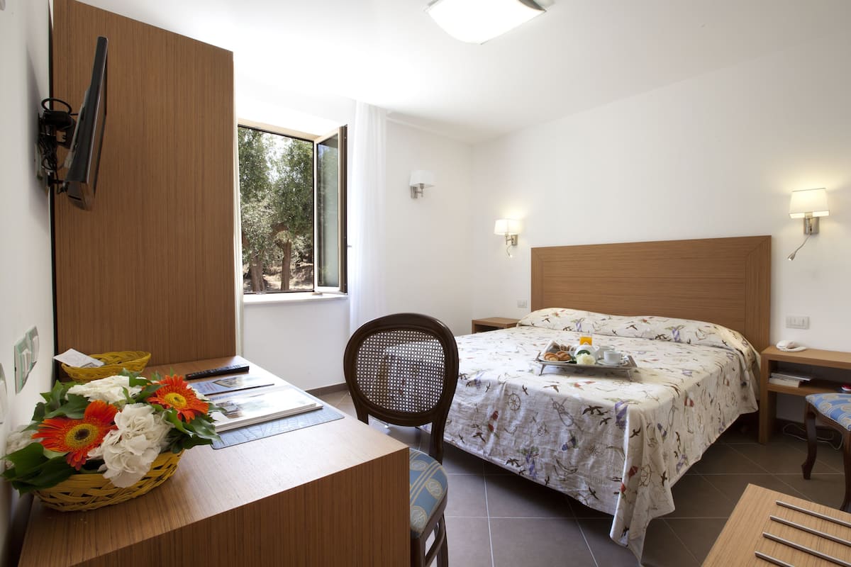 Ein Hotelzimmer mit Bett, Schreibtisch mit Blumenkorb, Sessel, Nachttisch und Beistelltisch.