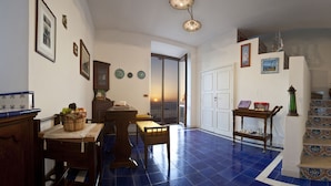 A dining area with a table set for two, a chair, and a basket of fruit. There is a staircase with decorative tiles leading to another room. - Villa Angelina (Massa Lubrense)