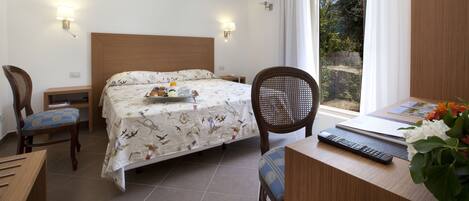 A hotel room with a bed, two chairs, a desk with a laptop and remote, and a window with curtains.