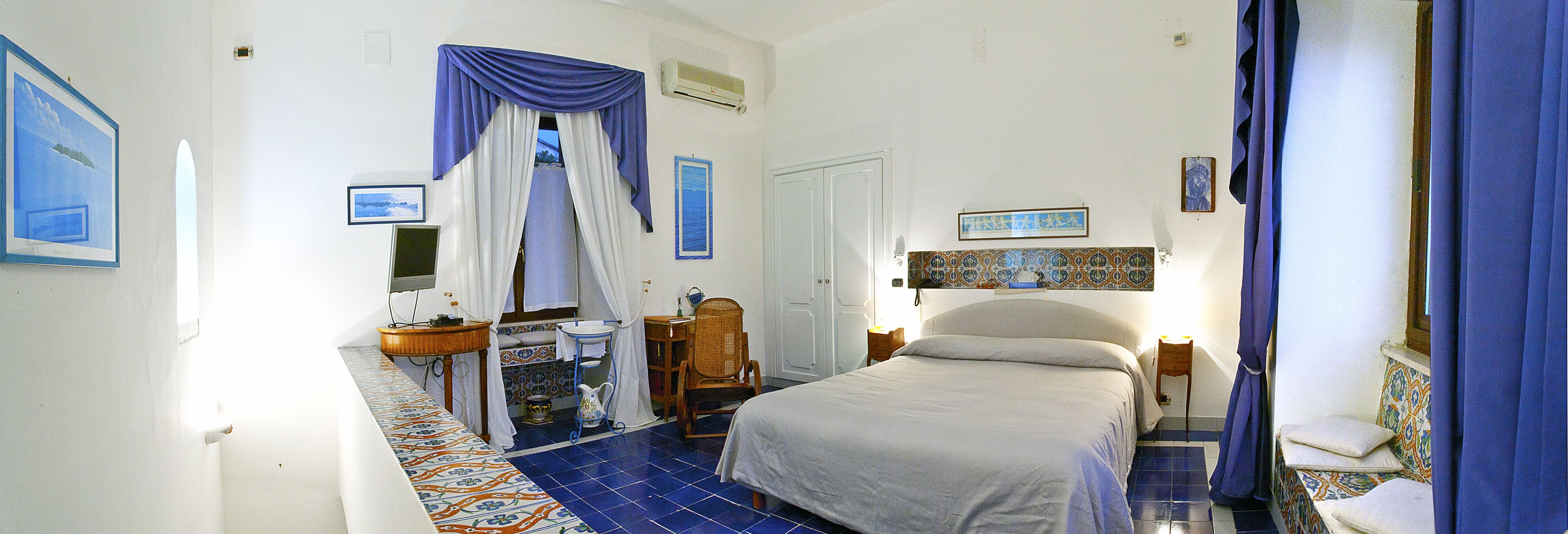 A bedroom with a bed, a chair, a small table, a mirror, and a window with curtains.