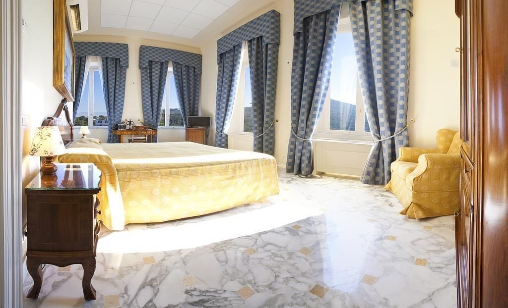A spacious bedroom with a large bed, a wooden nightstand, a desk with a lamp, and a chair.