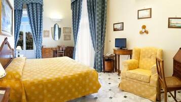 A hotel room with a bed, a chair, a desk with a computer, and a window with curtains.