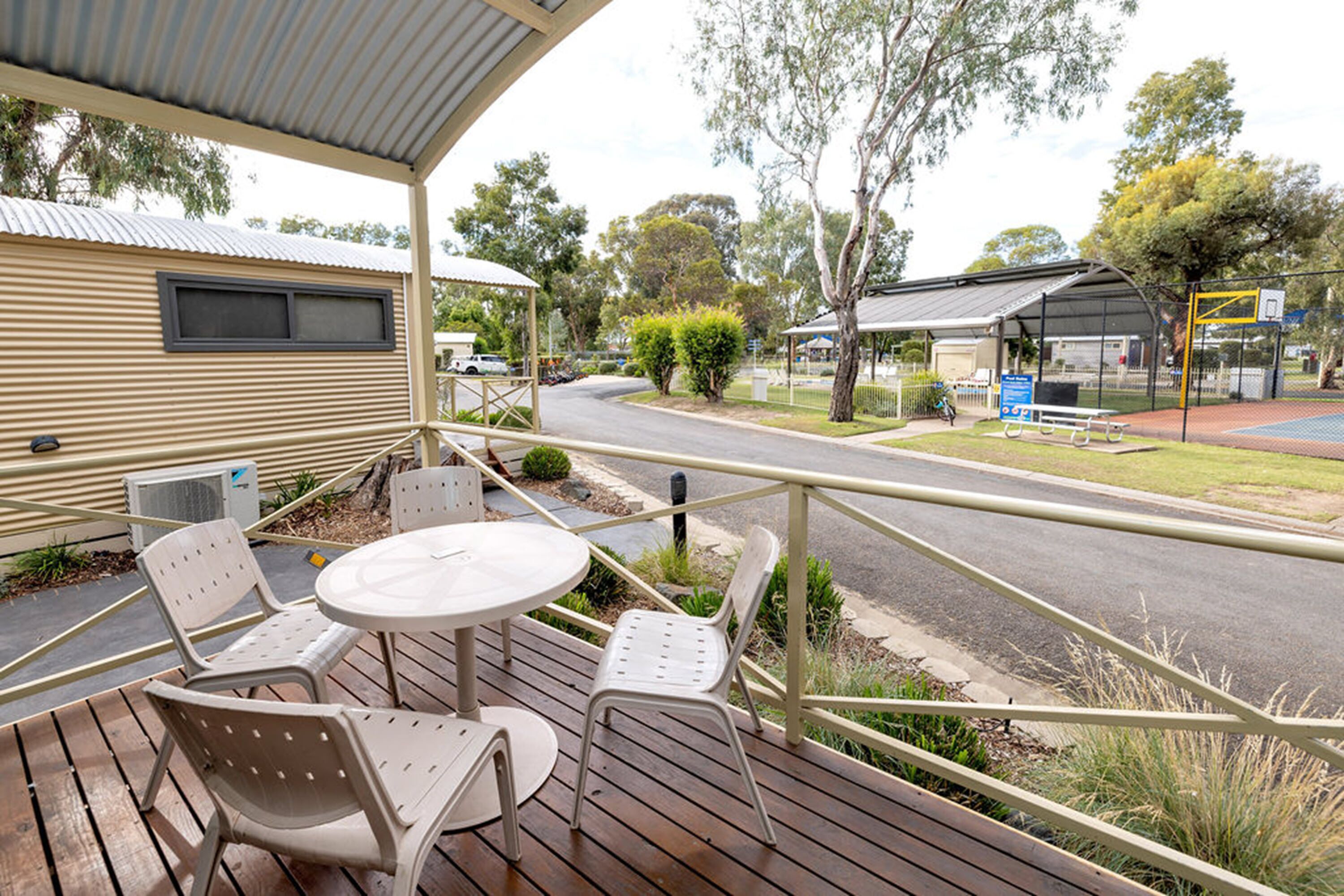 A covered outdoor area with a table and chairs, a view of a road, and a building with a metal roof.