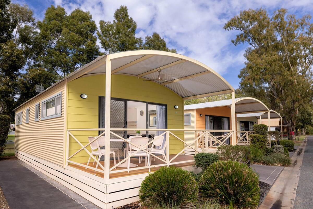 A mobile home with a covered porch, a dining area, and a small garden.