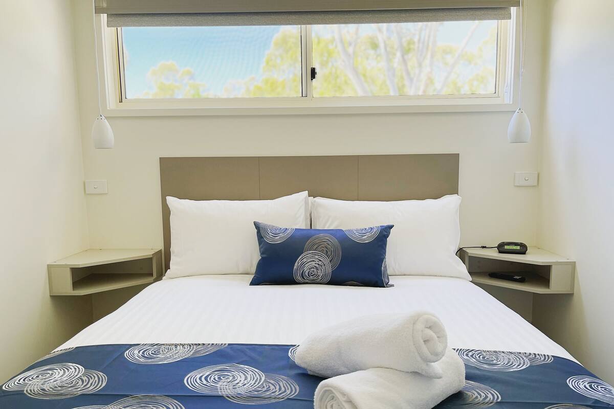 A neatly made bed with a blue and white patterned bedspread, two pillows, and rolled towels.